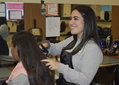 One girl is seen smiling while styling a girl's hair