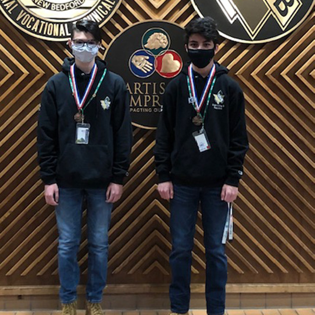 Students standing in front of a wall with the GNBVT logo on it