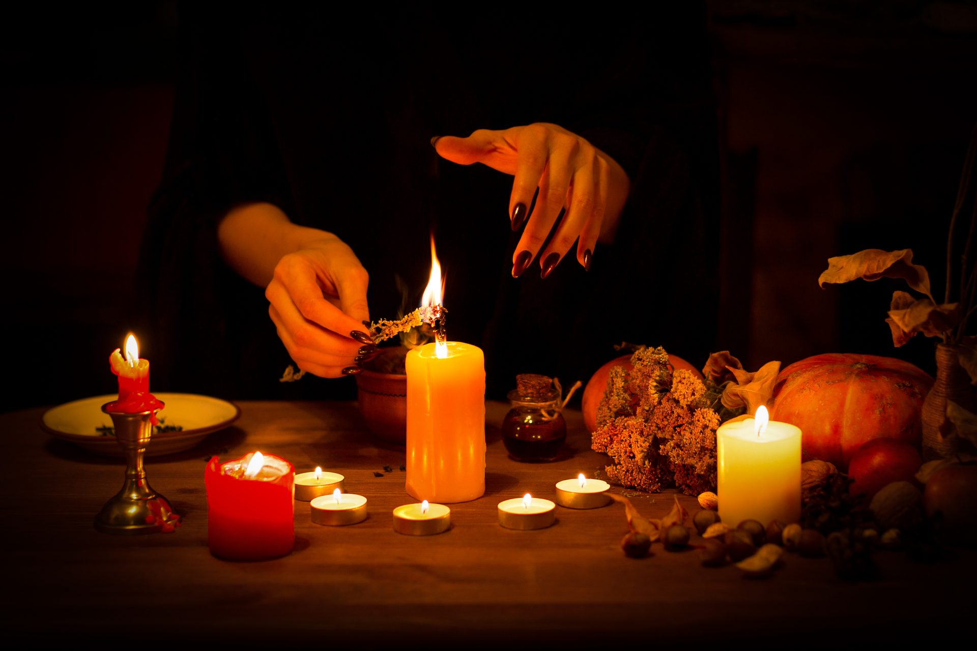 Witch burns a herb on the altar in the dark. Female hands with sharp black nails do magic among candles, pumpkin, nuts, dry leaves, selected focus, low key