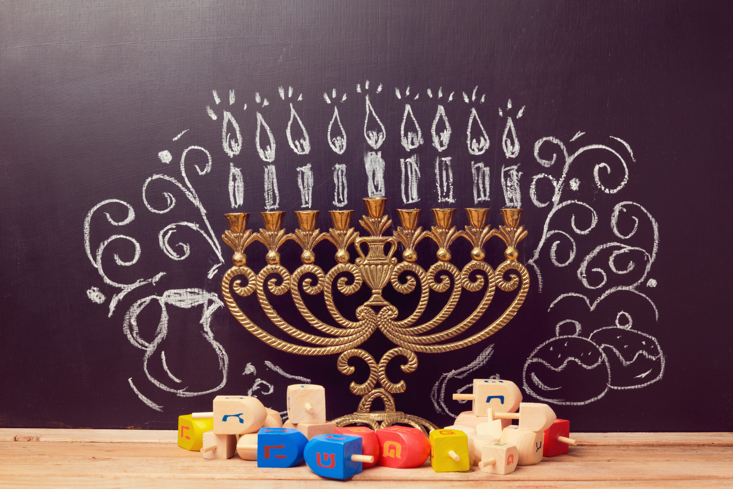 Creative Jewish holiday Hanukkah background with menorah and spinning tops over chalkboard with hand drawing