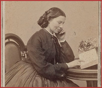 old photograph of a woman (clara harlowe Barton) sitting at a table in medical attire reading a book