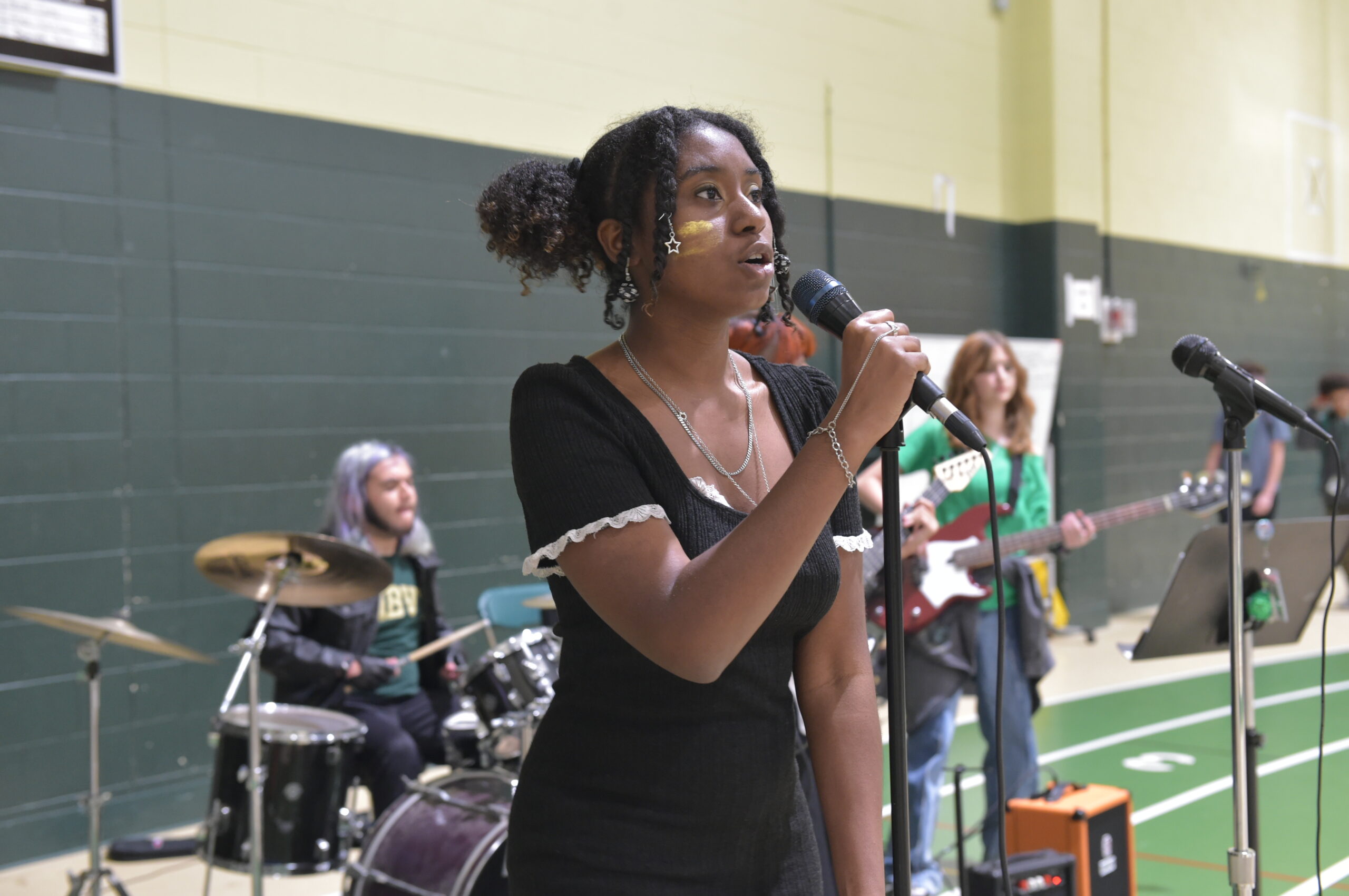 Girl singing with a microphone in her hand with students in the background playing a variety of different instruments